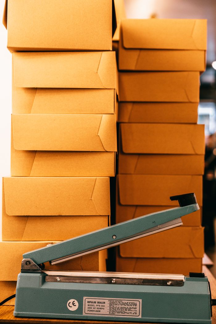 Bag sealer with information on sticker near heaps of similar carton boxes in industrial building